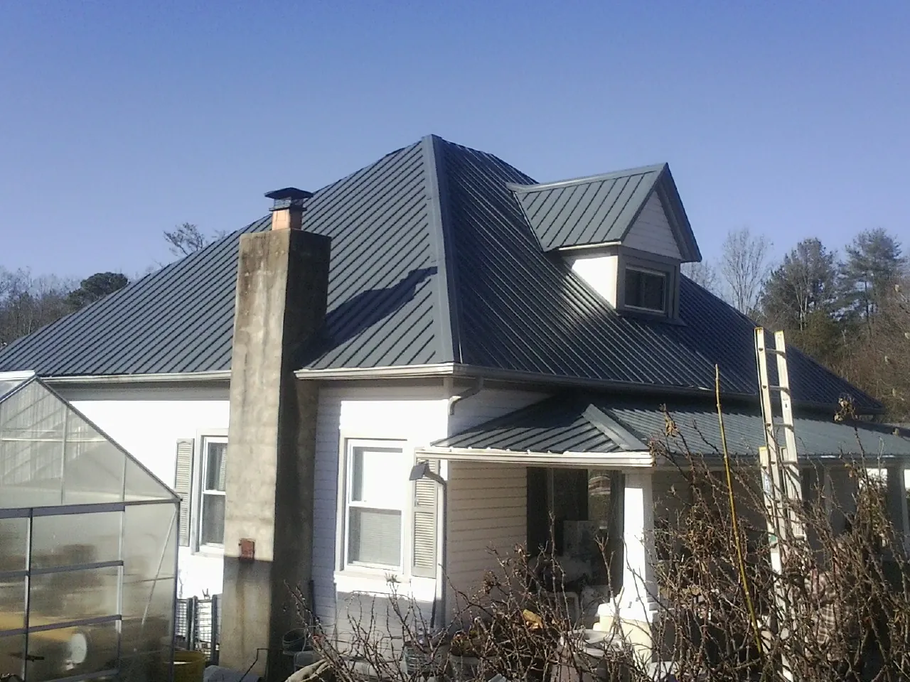 Dark blue standing seam metal roof on a white farmhouse with dormer — Slate & Tile Roof Repair by Roofing Brothers in Harmony