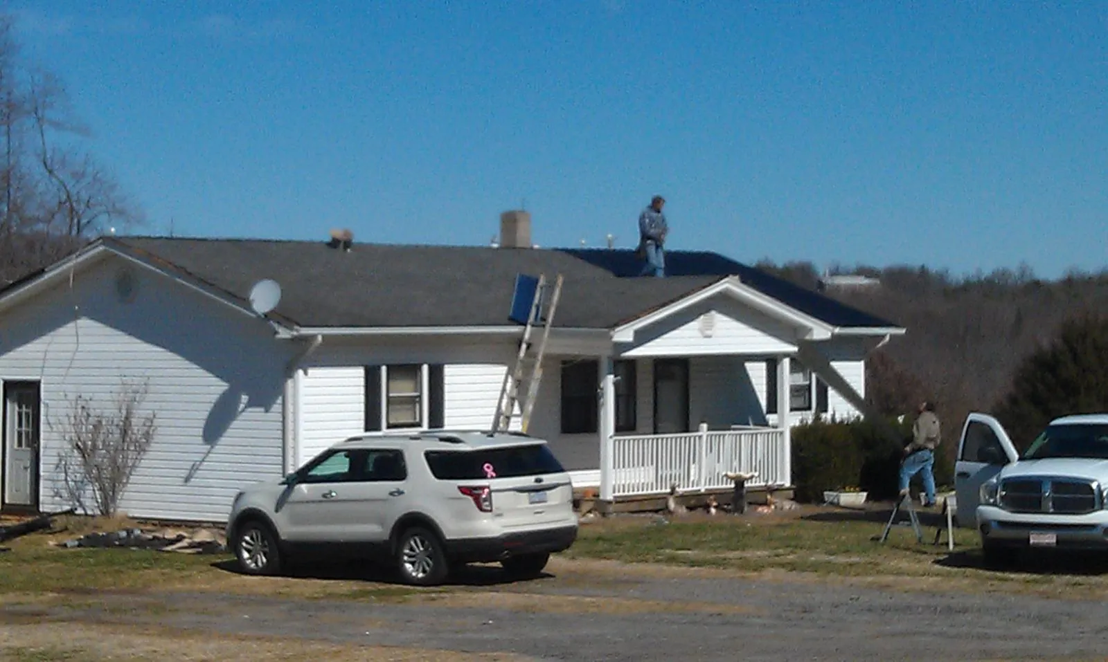 Roofers stripping shingles from a white ranch house roof in Harmony