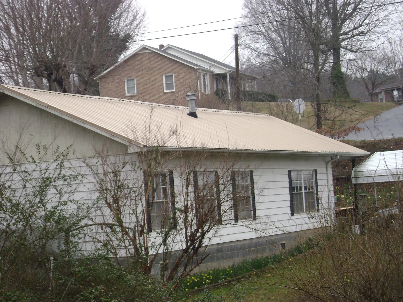 Tan metal roof on a white sided house set into a hillside — Commercial Roofing by Roofing Brothers in Harmony